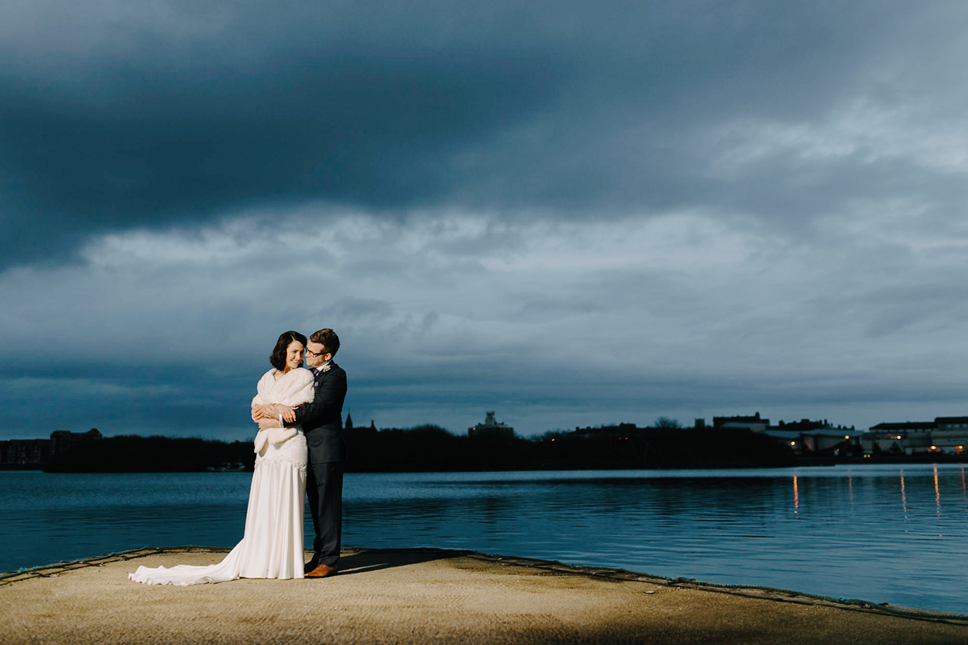 wedding photo of couple embracing next to a lake.