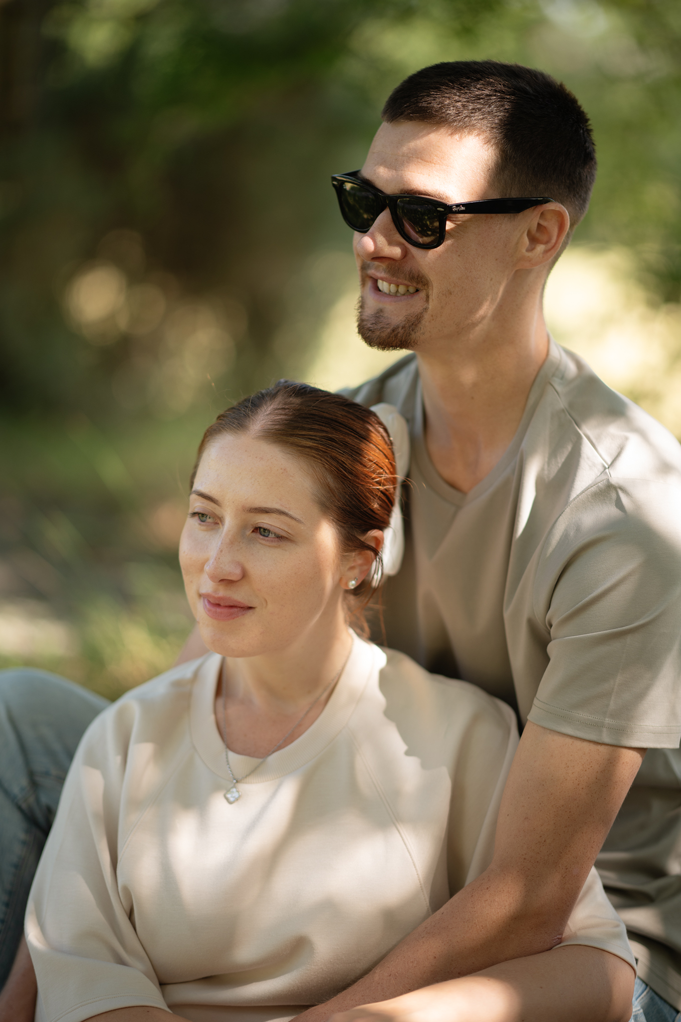Couple embracing and looking off-frame during a pre-wedding portrait session in woodland near Machynlleth, Powys.