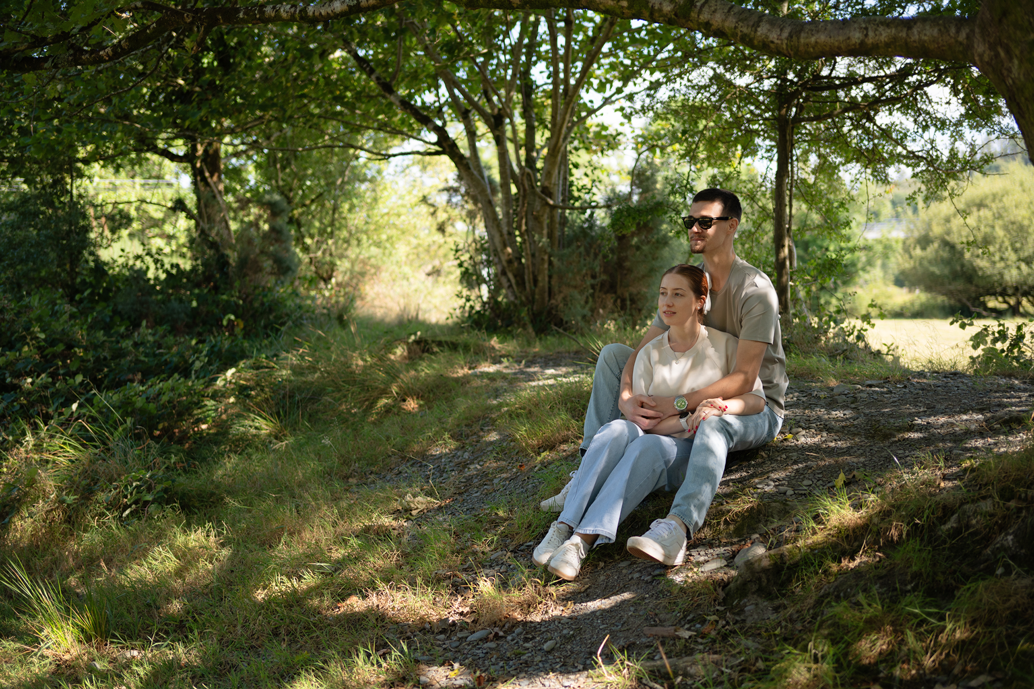 Couple sitting together on a gravel path beneath trees during a pre-wedding portrait shoot in Machynlleth, Mid Wales.
